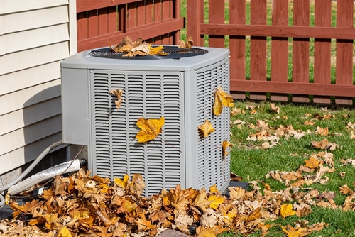 An outdoor HVAC unit is covered in leaves and needs cleaning.